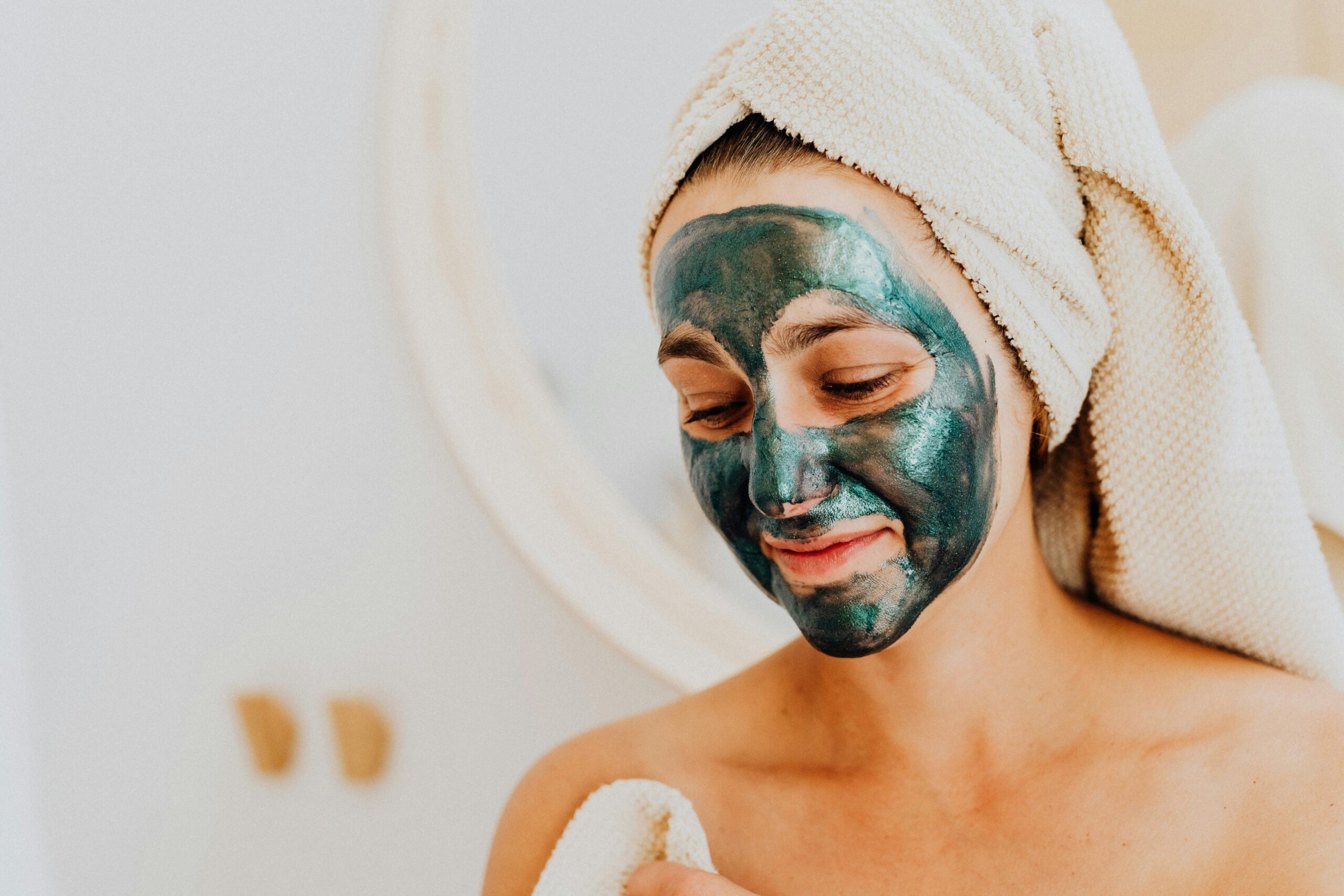 Woman applying a green facial mask for a relaxing skincare routine indoors.